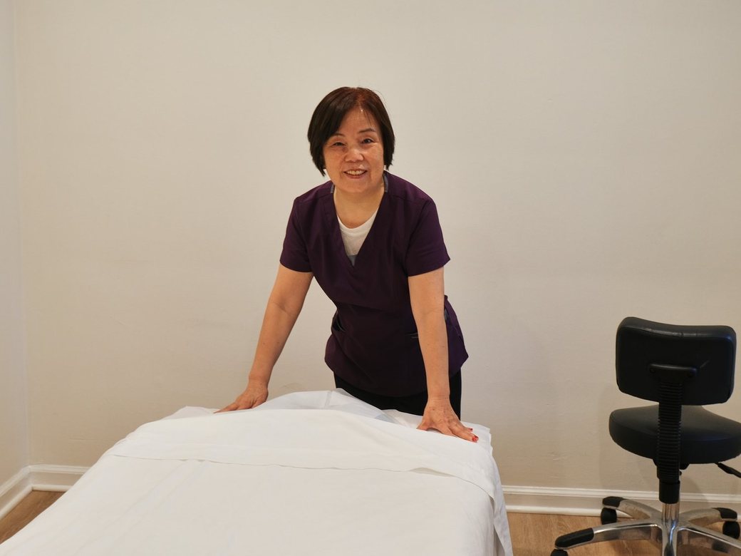 A smiling practitioner welcoming patients beside a prepared treatment table at Haram