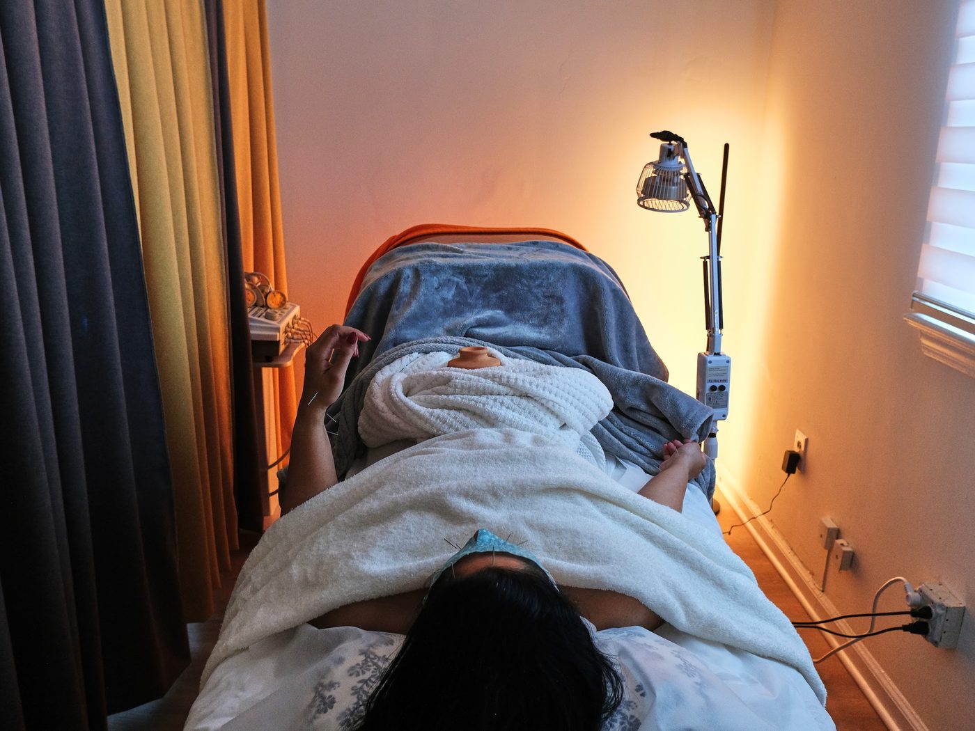 A patient resting under a warm lamp and drape in a treatment room